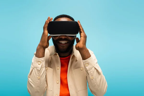 Cheerful african american man adjusting vr headset while gaming isolated on blue — Stock Photo