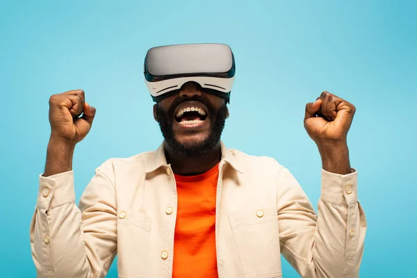 Afrikanisch-amerikanischer Mann schreit und zeigt Erfolgsgeste beim Spielen in vr Headset isoliert auf blau — Stockfoto