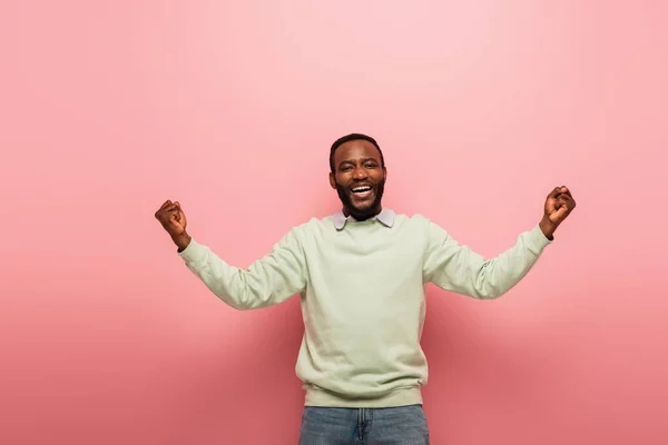 Excited african american man showing win gesture while smiling at camera on pink background — Stock Photo