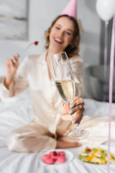 Mulher desfocada segurando copo de champanhe enquanto celebra aniversário no quarto — Fotografia de Stock