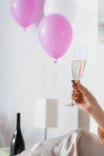 Cropped view of woman in pajama holding glass of champagne near blurred balloons — Stock Photo