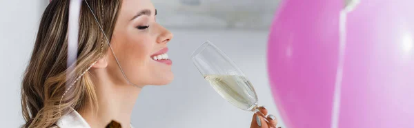 Side view of smiling woman holding champagne near balloon, banner — Stock Photo