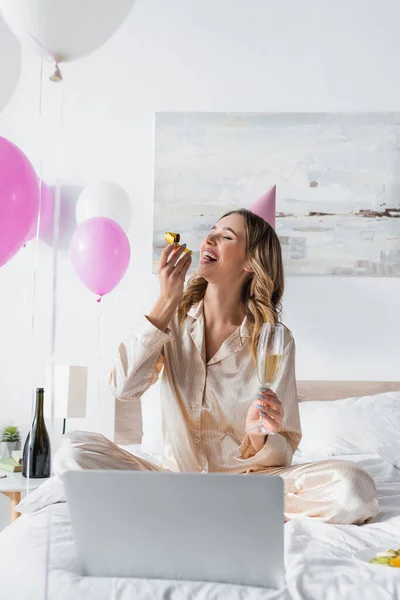 Mujer positiva celebrando cumpleaños cerca del ordenador portátil y globos en el dormitorio - foto de stock