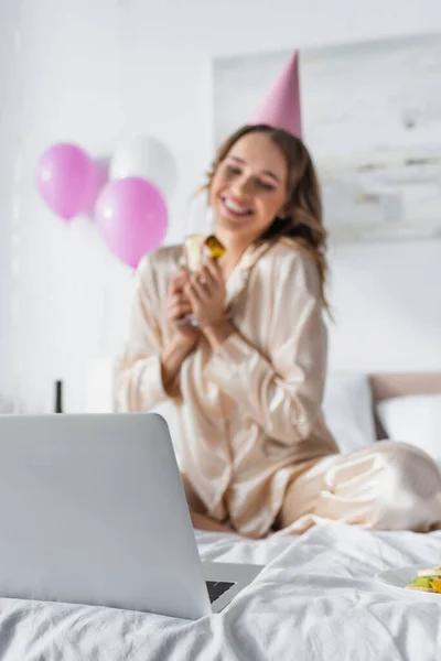 Laptop vicino donna sorridente che celebra il compleanno su sfondo sfocato in camera da letto — Foto stock