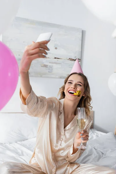 Mujer sonriente con champán tomando selfie durante la fiesta de cumpleaños en casa - foto de stock