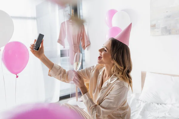 Vista laterale di donna allegra con champagne scattare selfie su smartphone in camera da letto — Foto stock