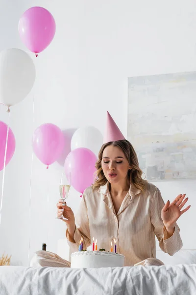 Woman with champagne blowing out candles on birthday cake on bed — Stock Photo