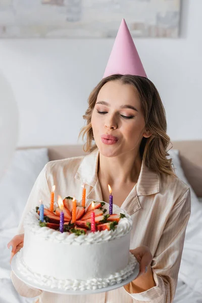 Mujer soplando velas en pastel de cumpleaños en el dormitorio durante la fiesta - foto de stock