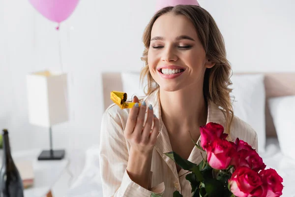 Glückliche Frau mit Partyhorn und Blumen feiert Geburtstag im Schlafzimmer — Stockfoto