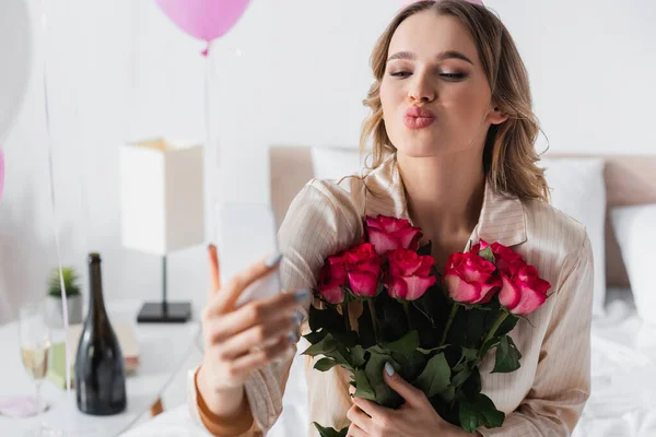 Mujer con rosas tomando selfie en smartphone y haciendo pucheros en casa - foto de stock