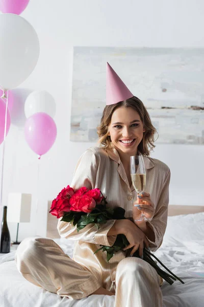 Frau im Pyjama hält Champagner und Rosen neben Luftballons im Schlafzimmer — Stockfoto
