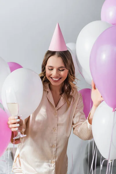 Mujer sonriente con champán de pie cerca de globos festivos en casa - foto de stock