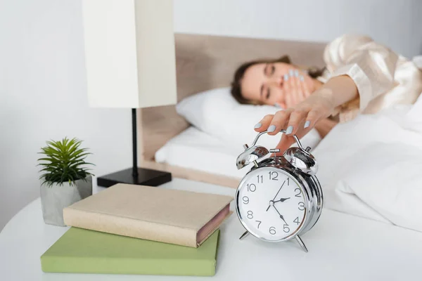 Verschwommene Frau hält Wecker in der Nähe von Büchern im Schlafzimmer — Stockfoto