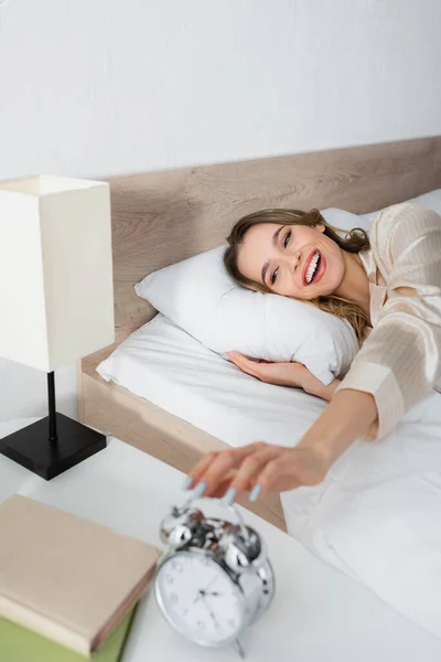 Mujer alegre tocando el reloj despertador borroso en el dormitorio - foto de stock