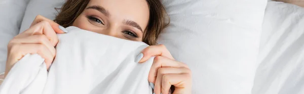 Vista superior de la mujer cubriendo la cara con manta y mirando a la cámara, pancarta — Stock Photo