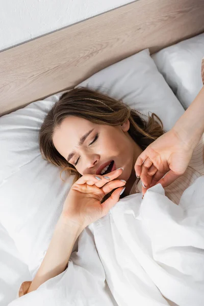 Top view of woman yawning on bed in morning — Stock Photo