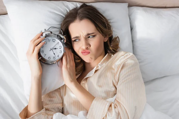 Top view of upset woman looking at alarm clock on bed — Stock Photo