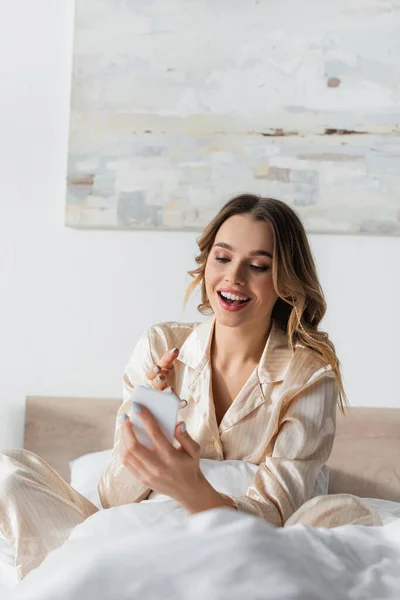 Счастливая женщина указывает на смартфон на кровати — Stock Photo