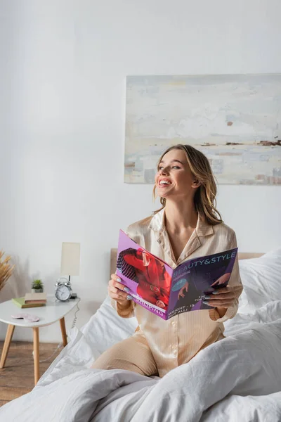 Улыбающаяся женщина в пижаме держит журнал на кровати — стоковое фото