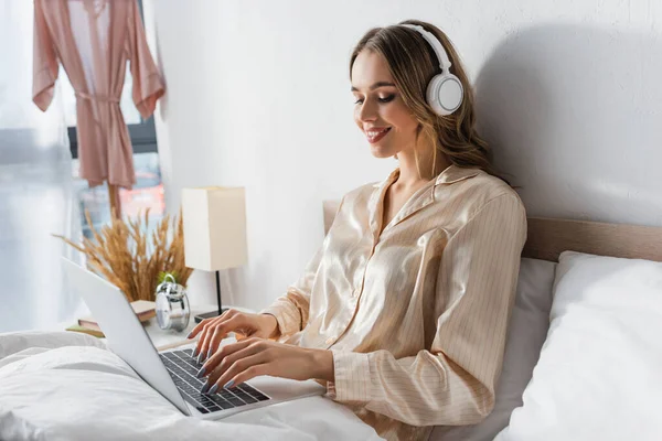 Усміхнений фрілансер в навушниках, використовуючи ноутбук у спальні — стокове фото