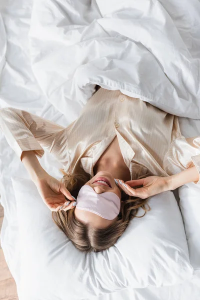 Draufsicht einer lächelnden Frau mit Schlafmaske auf dem Bett liegend — Stockfoto