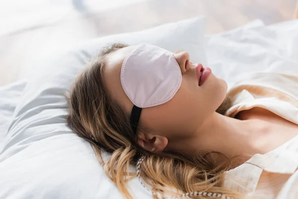 Mujer joven en la máscara de dormir sobre ropa de cama blanca - foto de stock