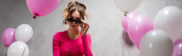 Стильна жінка тримає сонцезахисні окуляри біля повітряних куль, банер — стокове фото