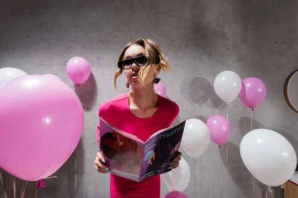 Frau mit Sonnenbrille hält Modemagazin in der Nähe von Luftballons — Stockfoto