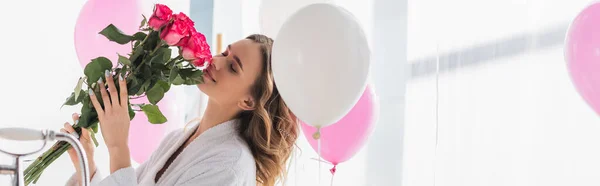 Woman in bathrobe smelling bouquet near balloons in bathroom, banner — Stock Photo
