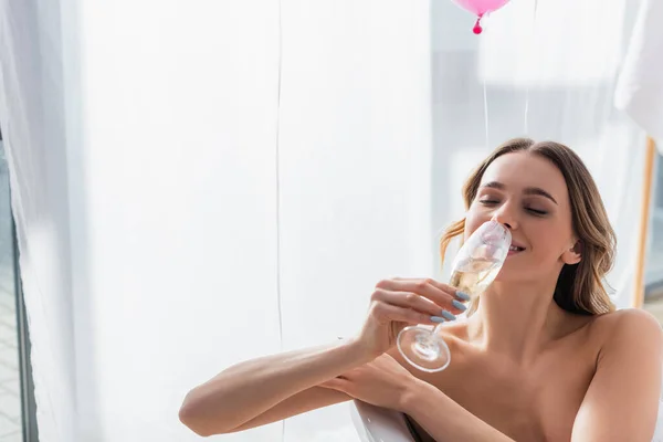 Femme souriante buvant du champagne dans la baignoire — Photo de stock