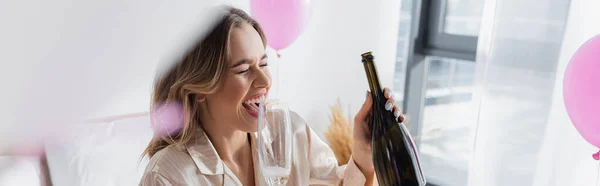 Fröhliche Frau mit Flasche und Glas Champagner in der Nähe von Luftballons im Schlafzimmer, Banner — Stockfoto