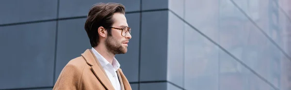 Seitenansicht des bärtigen Geschäftsmannes mit Brille und beigem Mantel, der nach draußen geht, Banner — Stockfoto