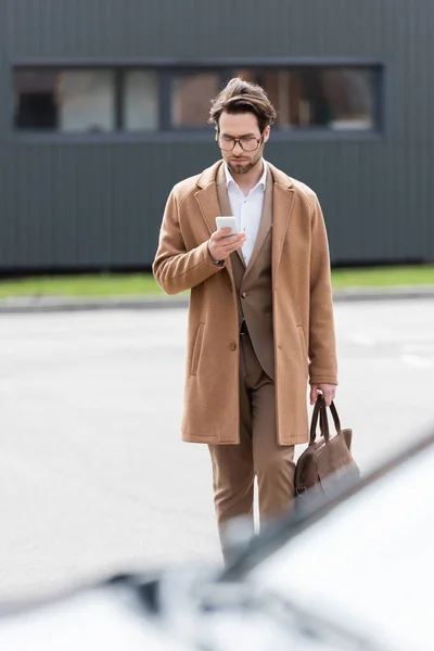Mann mit Brille und beigem Mantel mit Handy draußen — Stockfoto
