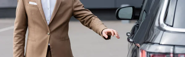 Обрізаний вид людини в бежевій куртці, що досягає дверей автомобіля, банер — стокове фото