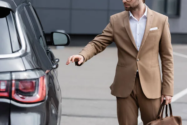 Vista parcial del hombre en traje beige y gafas que llegan a la puerta del coche - foto de stock