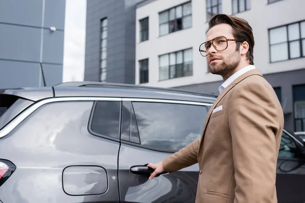 Jeune homme d'affaires en costume beige atteignant la porte de la voiture — Photo de stock