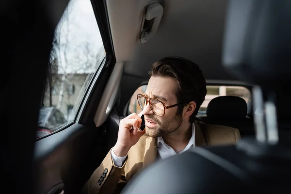 Unzufriedener Geschäftsmann im Anzug spricht auf Smartphone und blickt auf Autoscheibe — Stockfoto