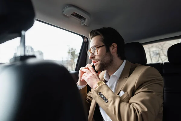 Uomo d'affari in giacca e cravatta che parla su smartphone e guarda il finestrino dell'auto — Foto stock