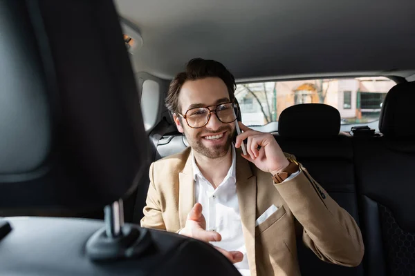 Homem alegre em terno e óculos falando no smartphone no carro — Fotografia de Stock
