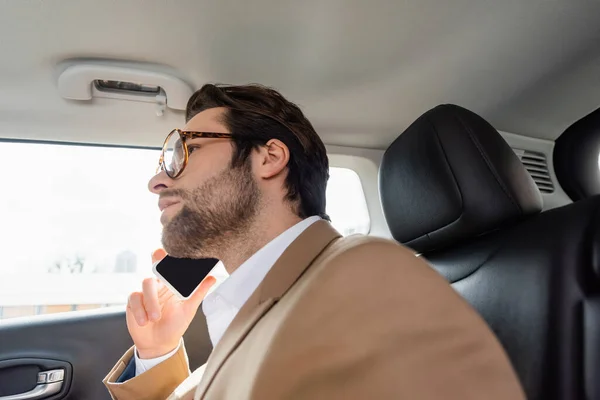 Inquiet homme en lunettes et costume parler sur smartphone en voiture — Photo de stock