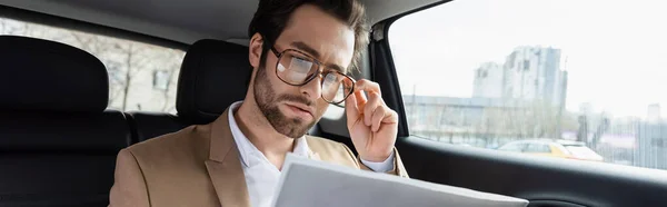 Hombre seguro de sí mismo ajustar gafas y leer el periódico de negocios en el coche, pancarta - foto de stock