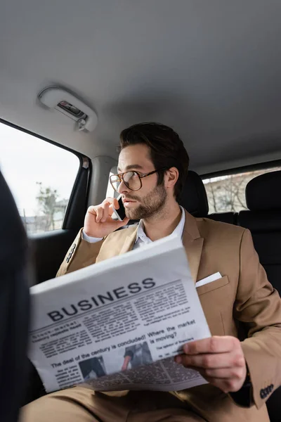 Homem confiante em óculos falando no smartphone e segurando jornal de negócios no carro — Fotografia de Stock