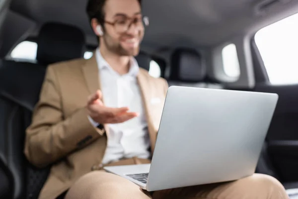 Verschwommener Geschäftsmann mit Brille und drahtlosen Kopfhörern bei Videoanruf im Auto — Stockfoto