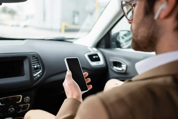 Blurred man in glasses holding smartphone with blank screen in car — Stock Photo