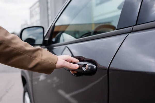 Vue recadrée de la main masculine atteignant la porte de la voiture brillante noire — Photo de stock