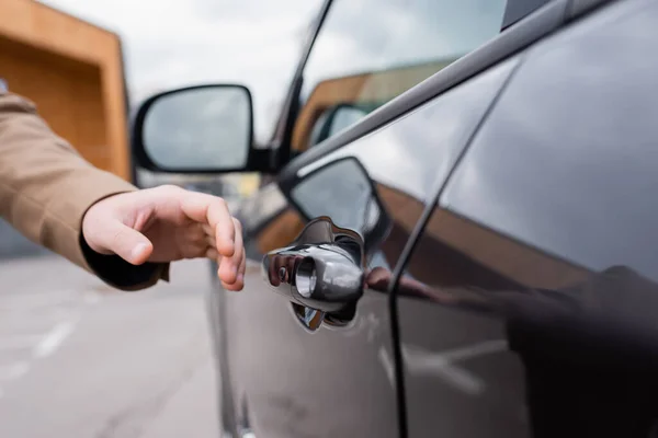 Vue recadrée de la main masculine atteignant la porte de la voiture noire sur le parking — Photo de stock