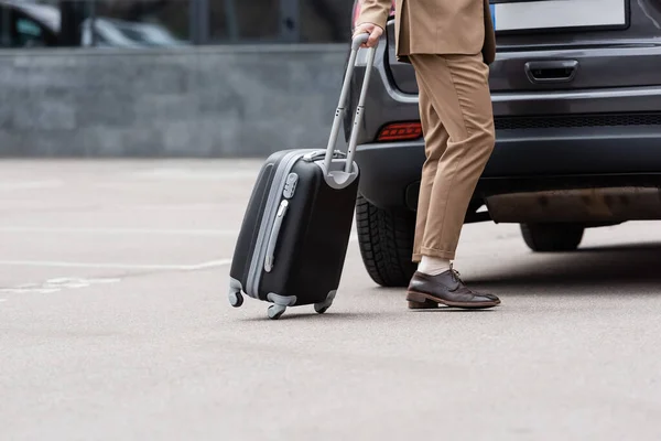 Vista recortada del hombre en traje caminando cerca del coche con la maleta - foto de stock