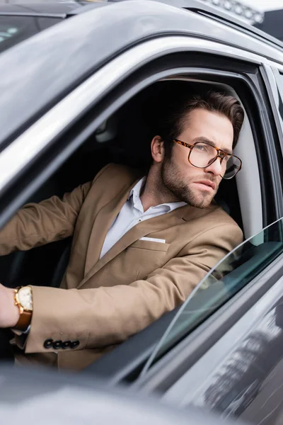 Bearded man in glasses looking through car window while driving auto — Stock Photo