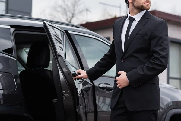 Visão parcial do guarda-costas barbudo com fone de ouvido de segurança abrindo porta do carro — Fotografia de Stock