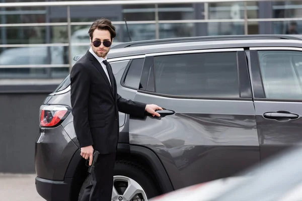 Safeguard in sunglasses and suit holding gun near modern auto — Stock Photo